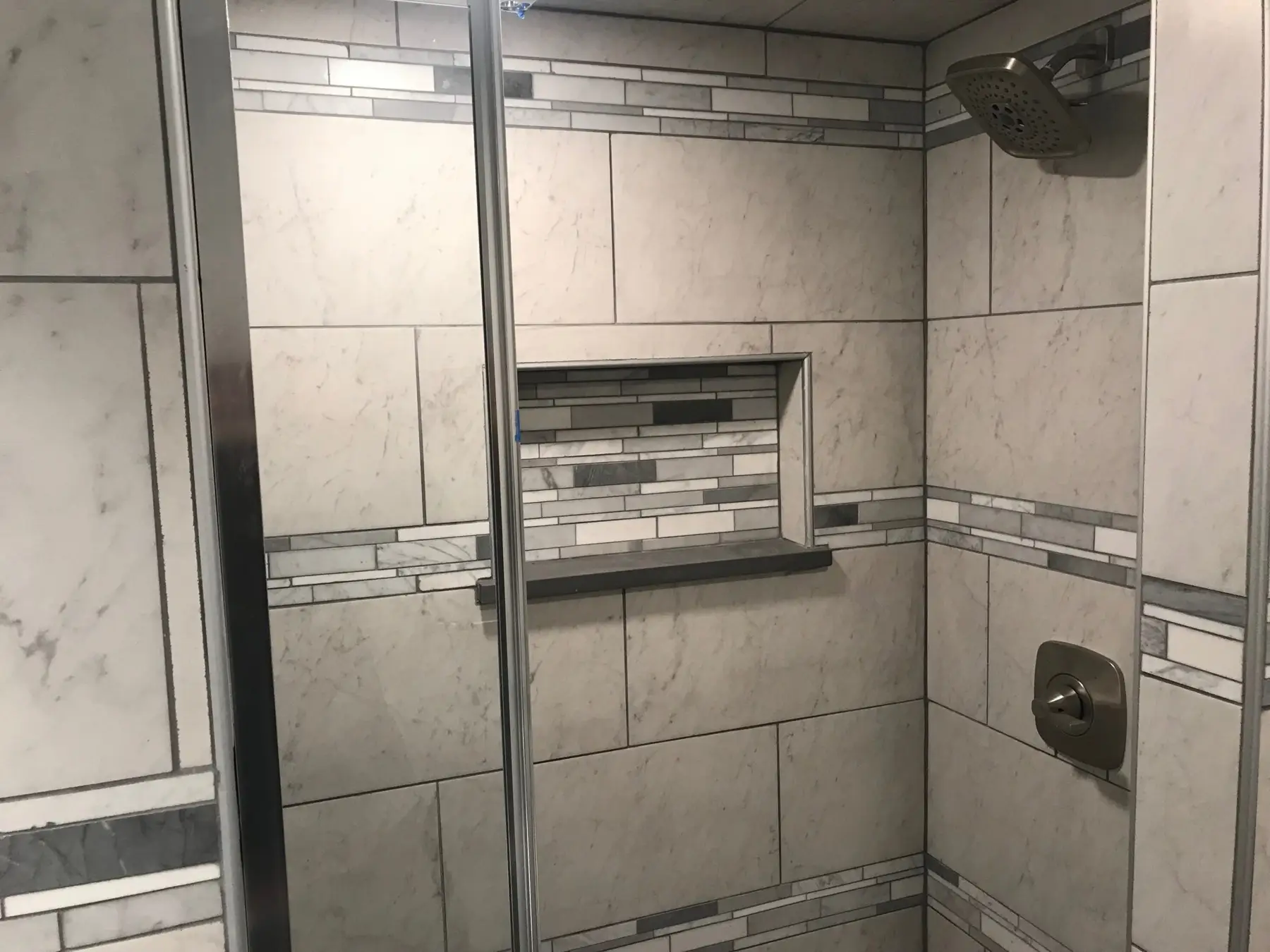 Tiled shower with a recessed light and a mosaic accent band.