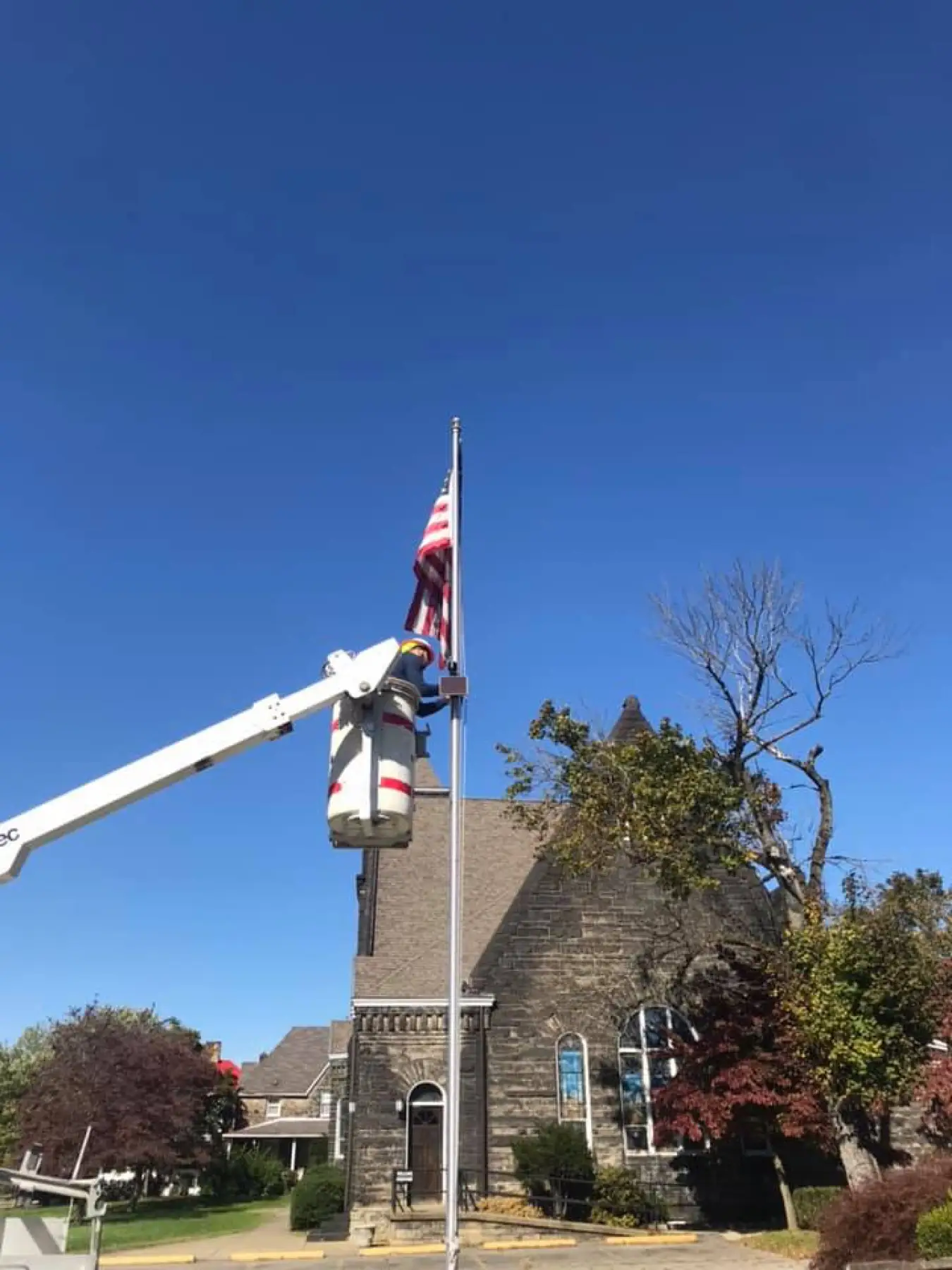 Bucket truck boom raised beside a stone church under a blue sky.