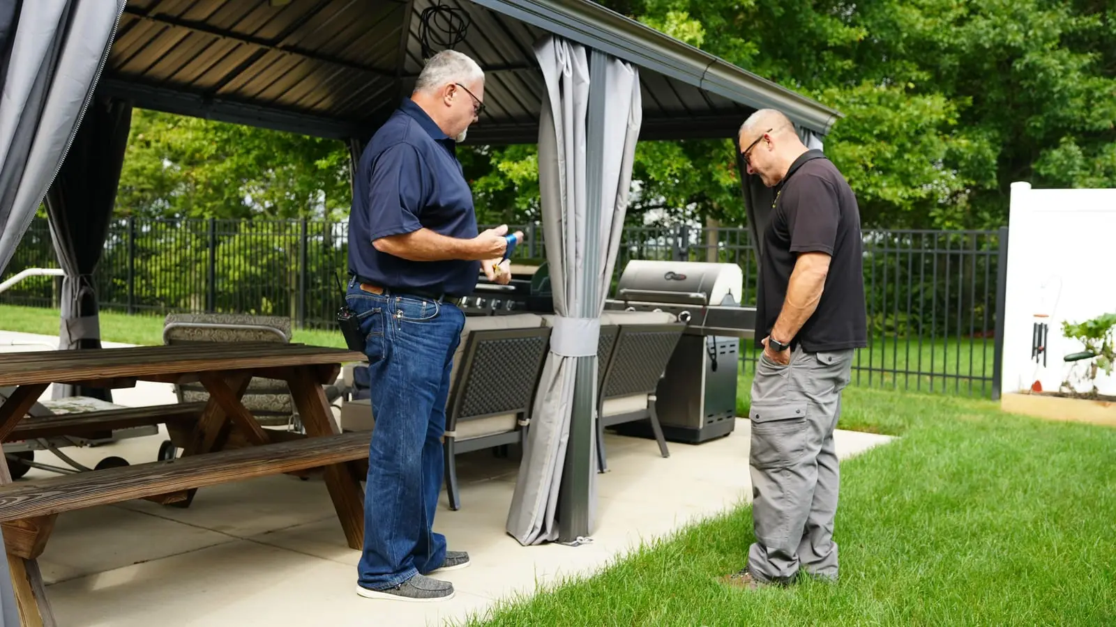 An Electric O electrician talking a homeowner through the job under a backyard gazebo.