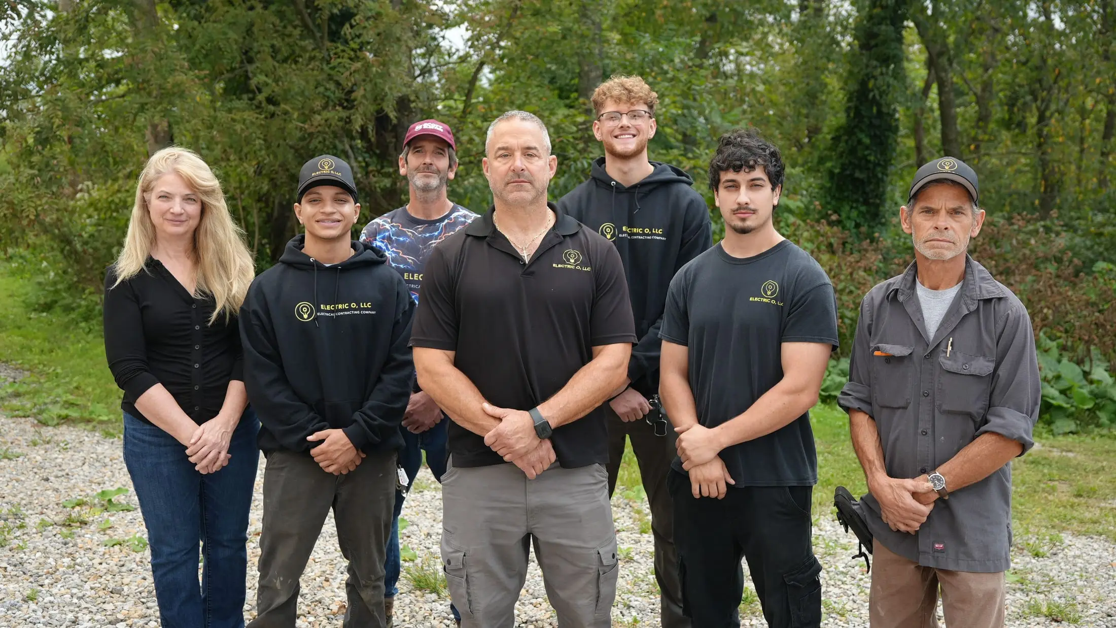 The seven people of Electric O standing together outdoors in branded Electric O shirts, hoodies and caps.