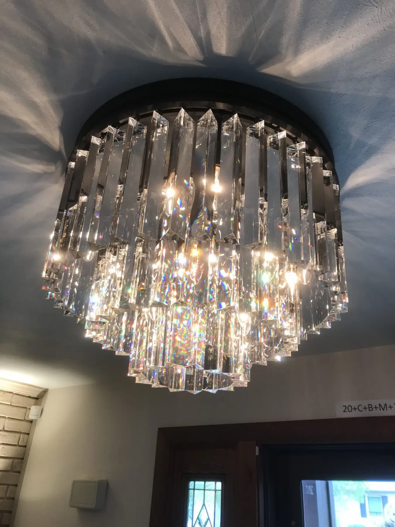 A tiered crystal chandelier lit in a dark ceiling.