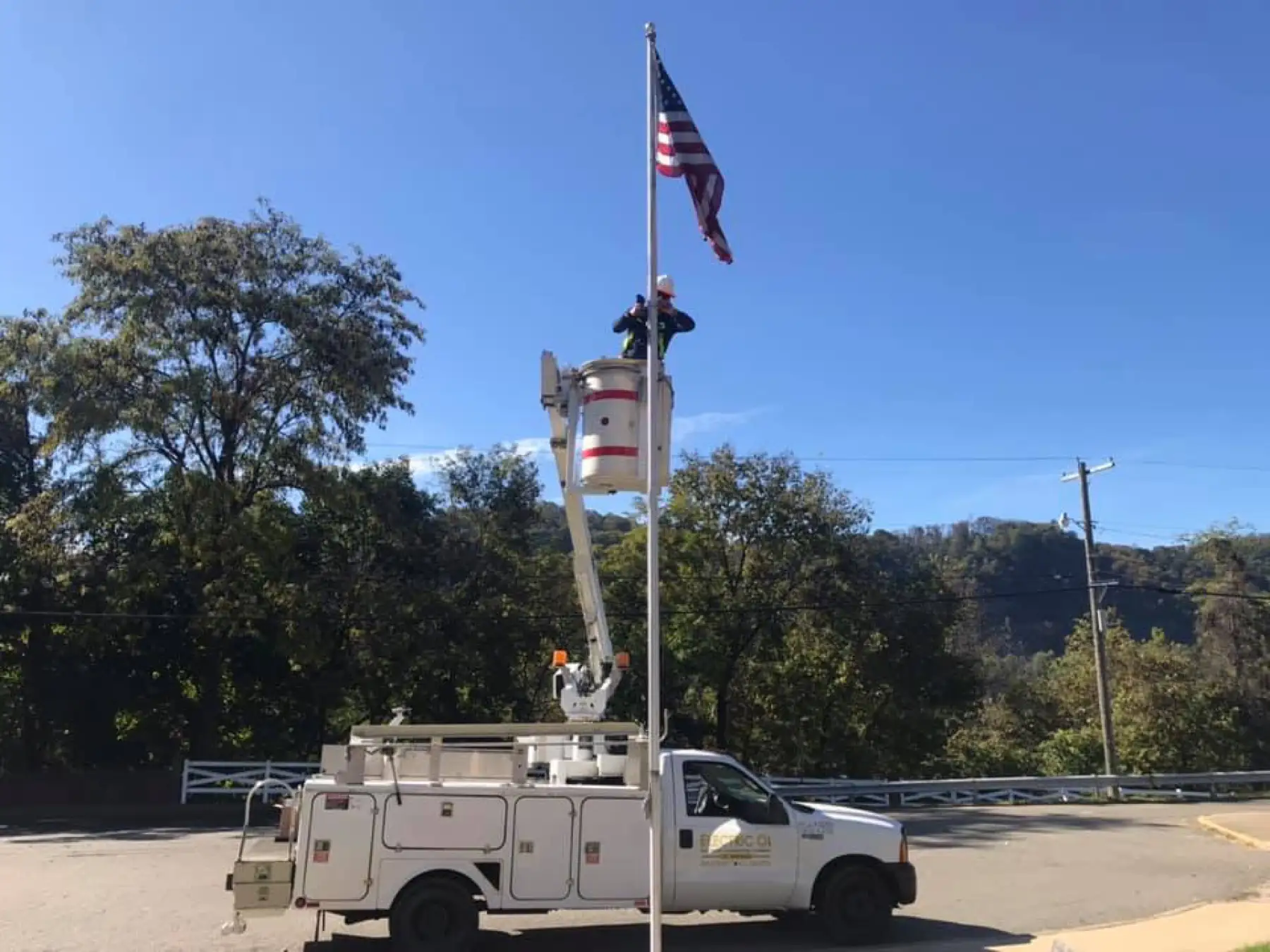 Bucket truck raised beside a flagpole flying the American flag.