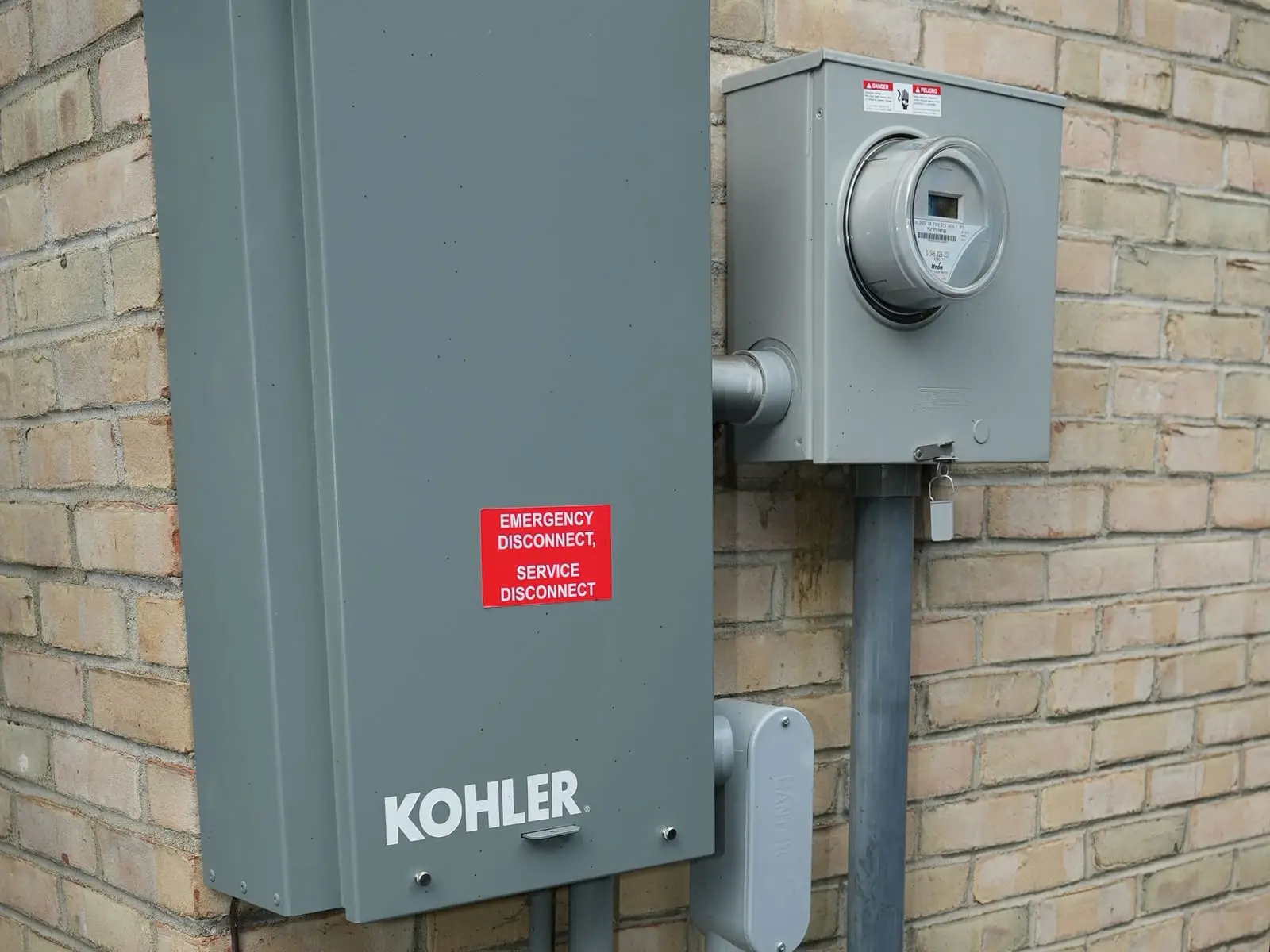 A gray Kohler service disconnect mounted on tan brick next to the electric meter, with conduit running down the wall.