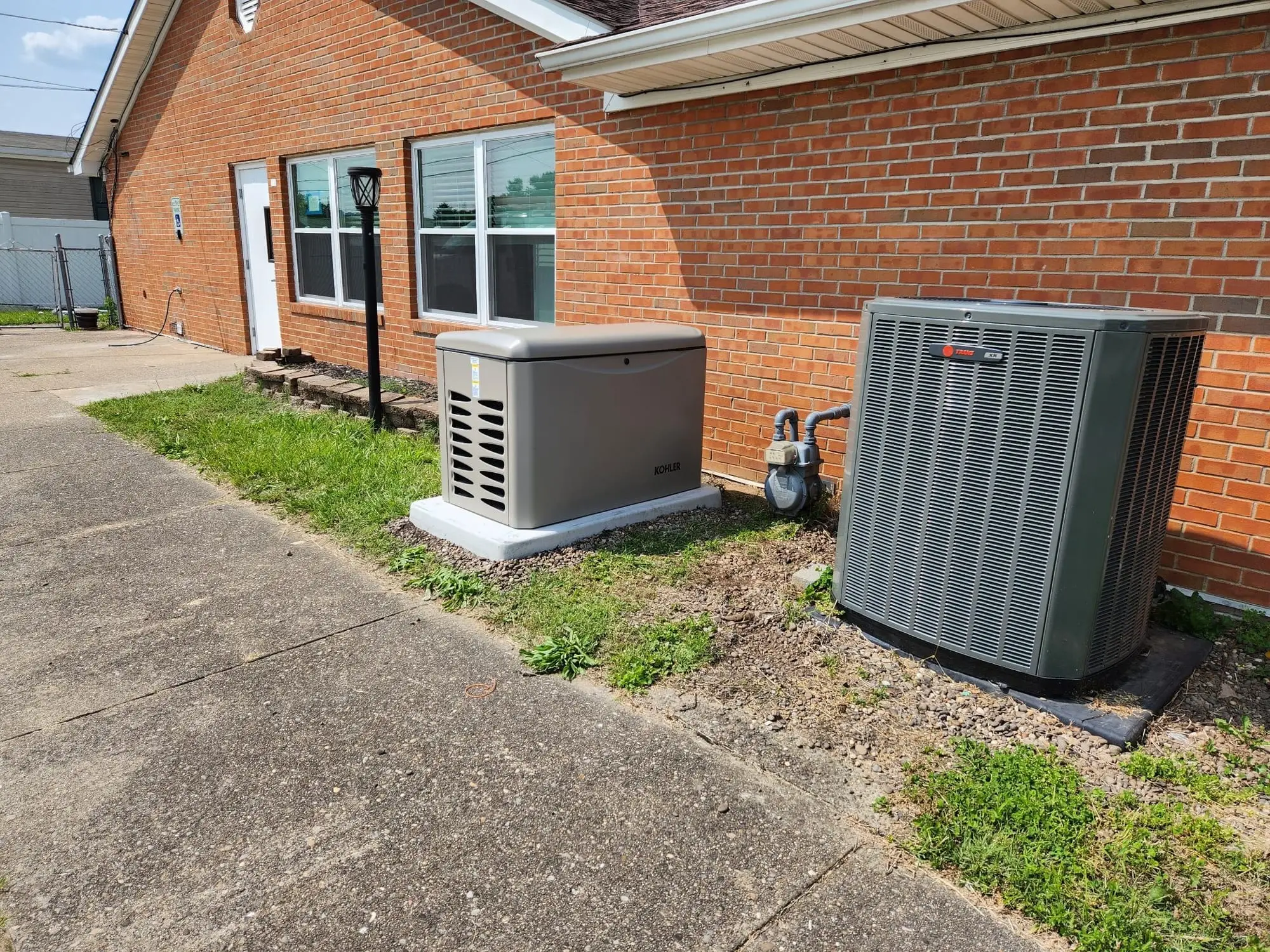 A Kohler standby generator on a concrete pad beside a brick house, with the air-conditioning condenser and gas meter next to it.