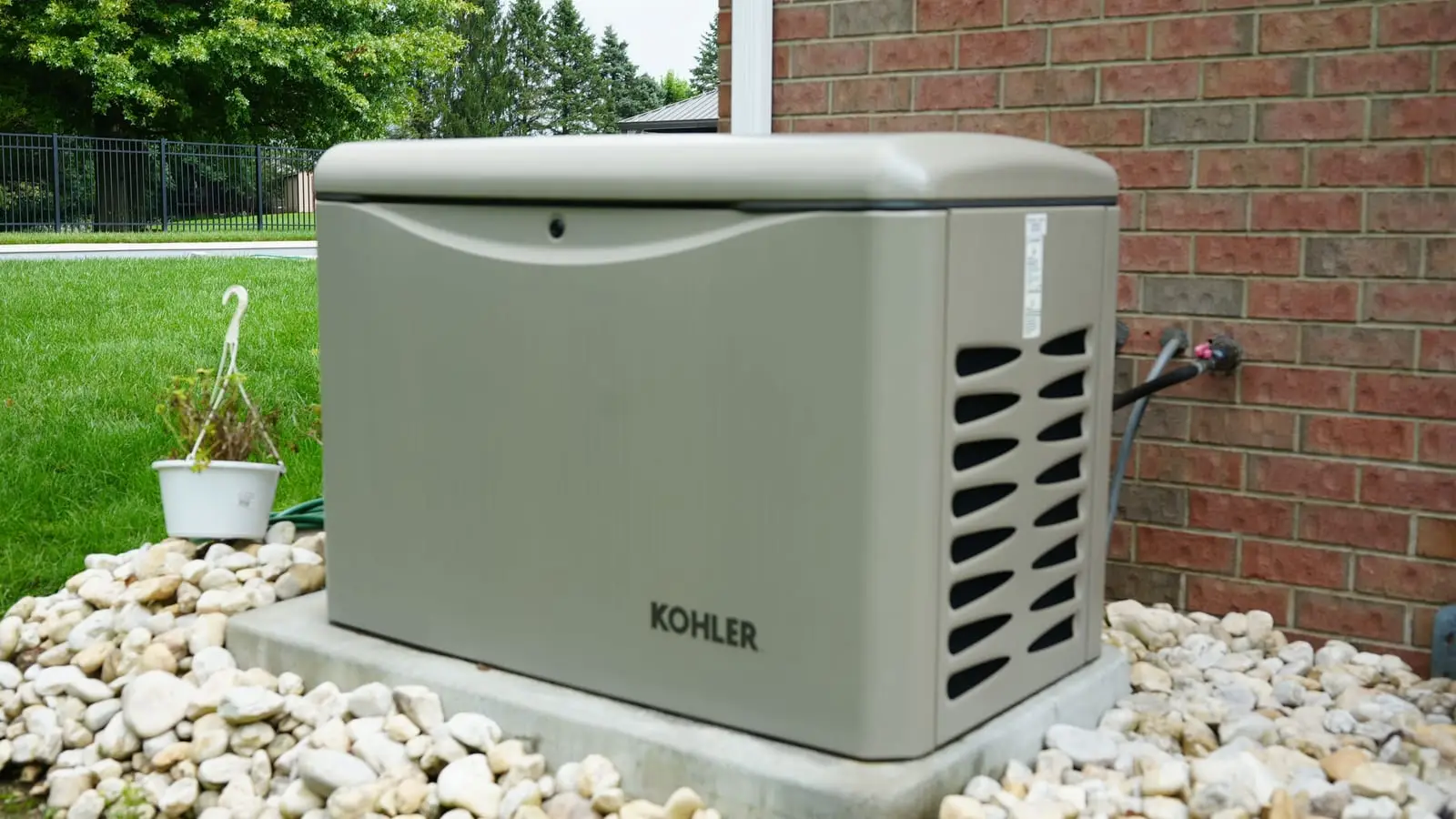A Kohler standby generator on a concrete pad in a river-rock bed beside a brick house, installed by Electric O.