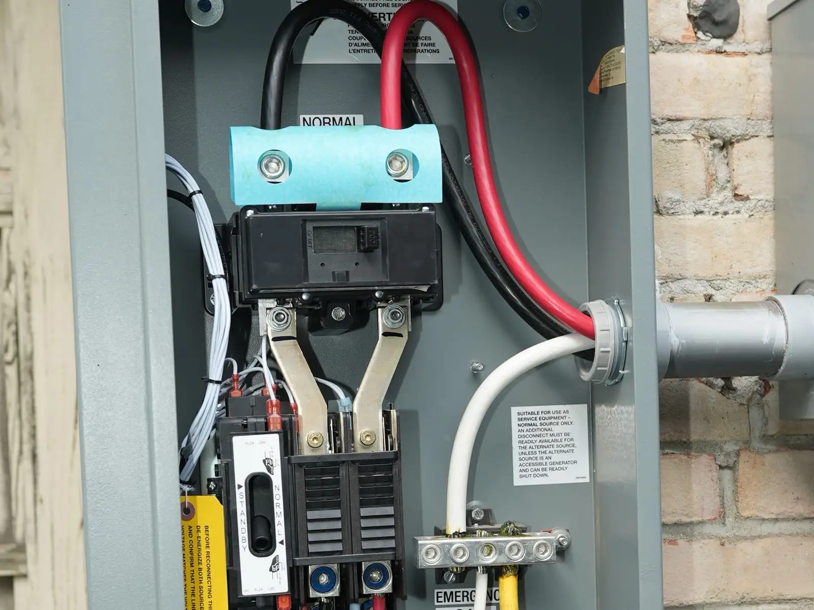 An open automatic transfer switch on a brick wall, its red, black and white conductors neatly routed and landed on the breakers.