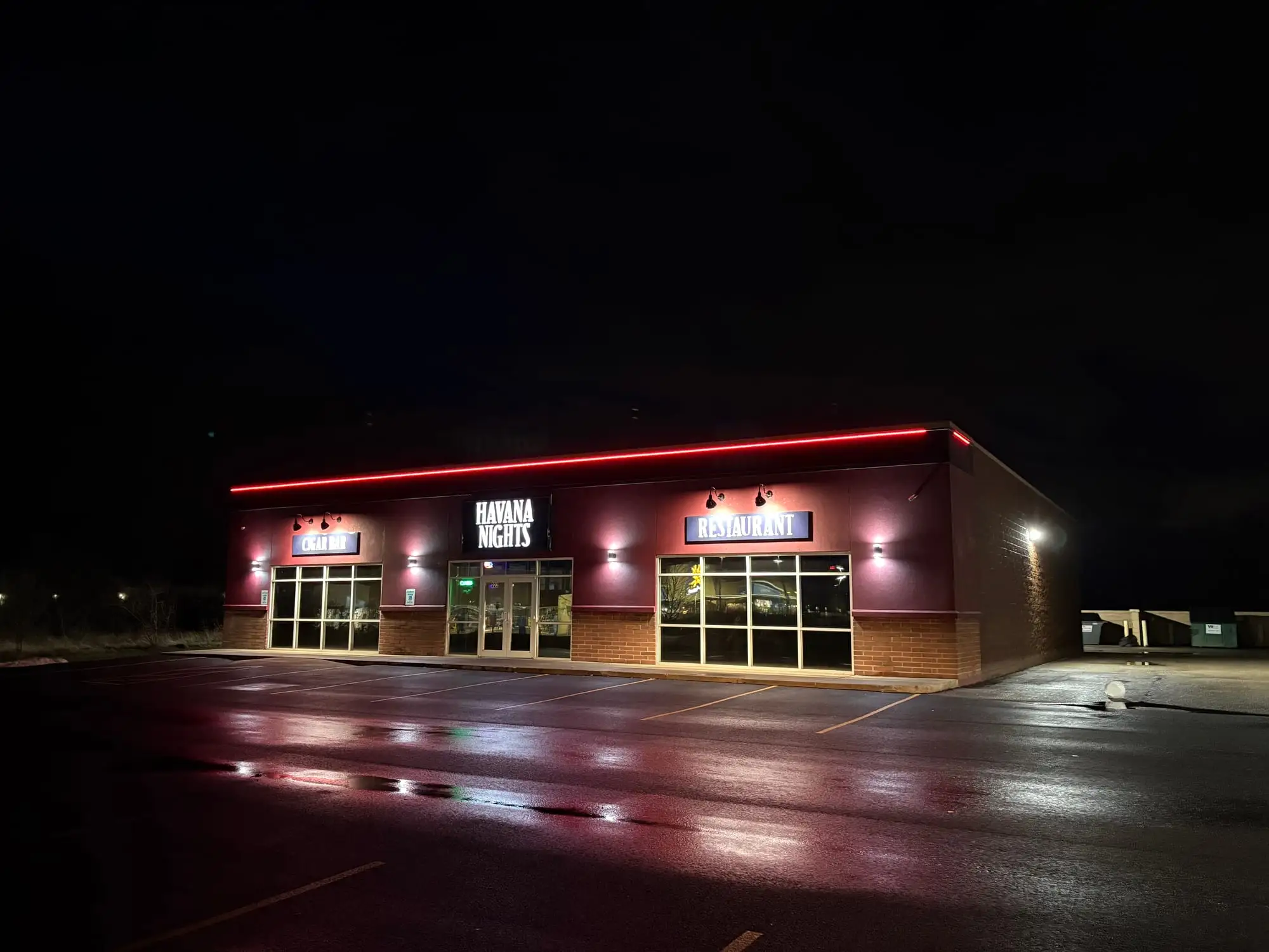 The Havana Nights cigar bar and restaurant at night, with a red LED roofline, lit signs and wall sconces.