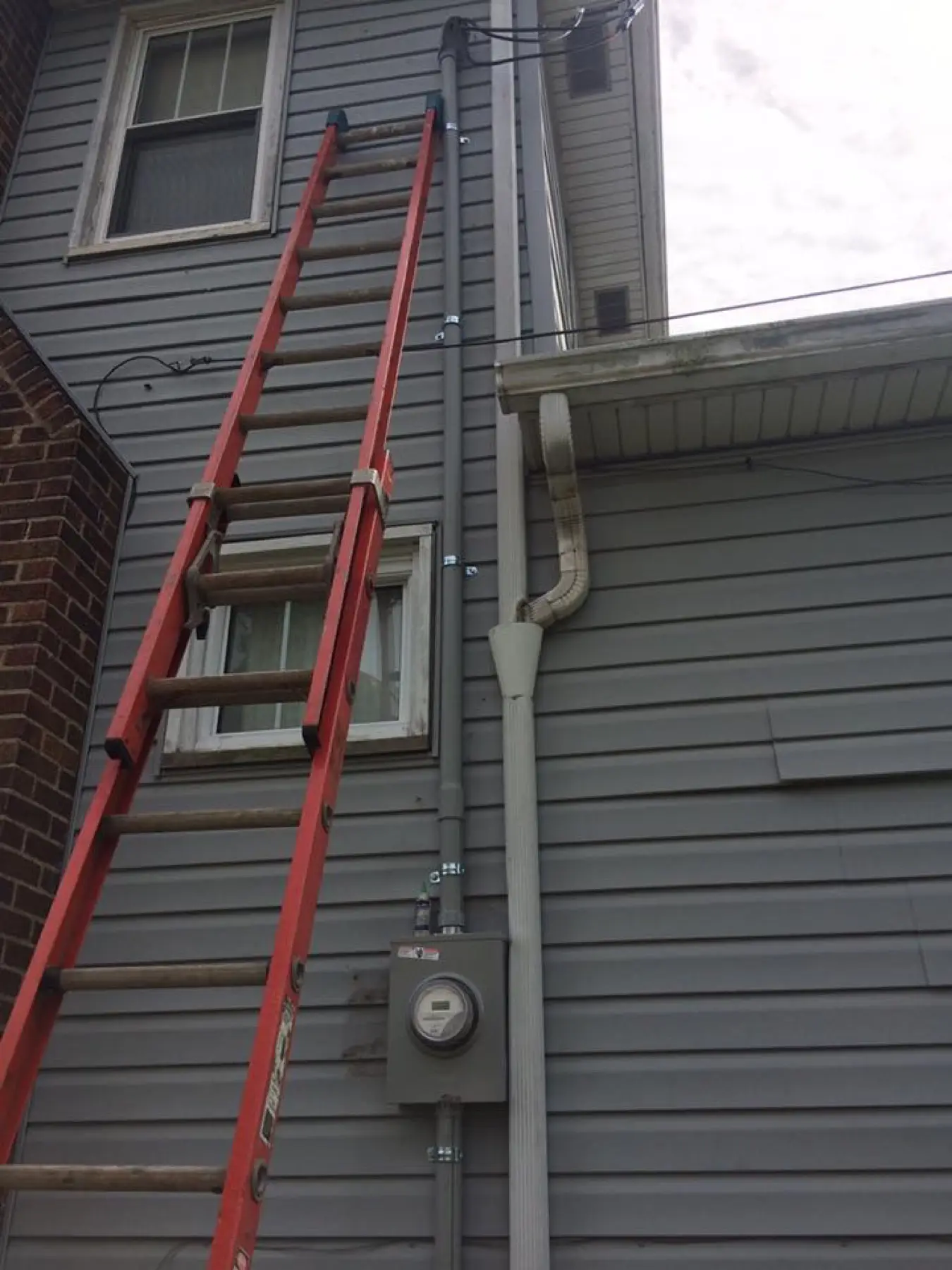 Ladder against siding beside the meter and service entrance.