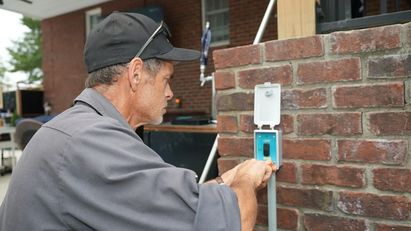 An Electric O electrician fitting a weatherproof switch cover on a brick pillar beside an outdoor patio.