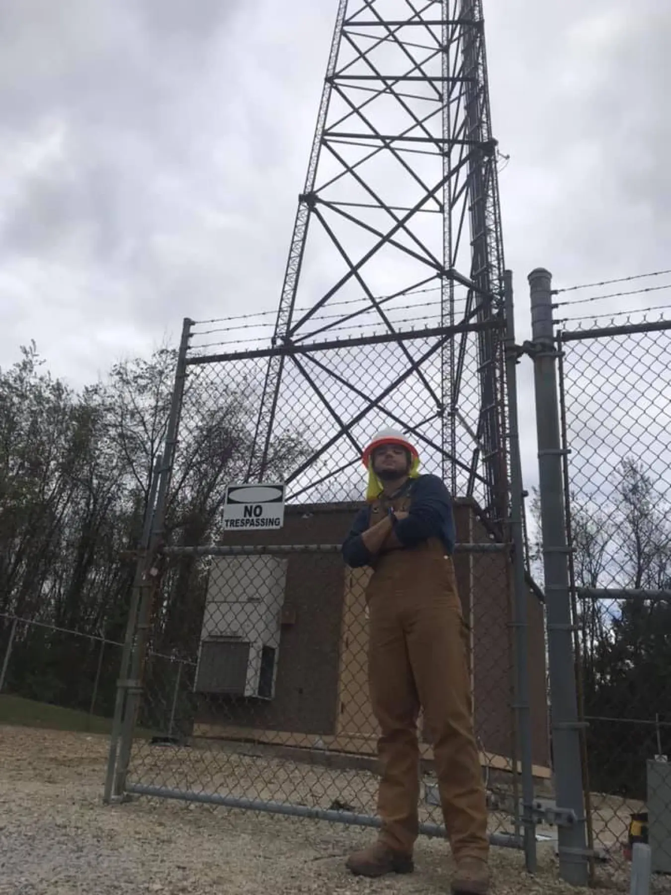 Electrician inside a chain-link enclosure at the base of a lattice tower.