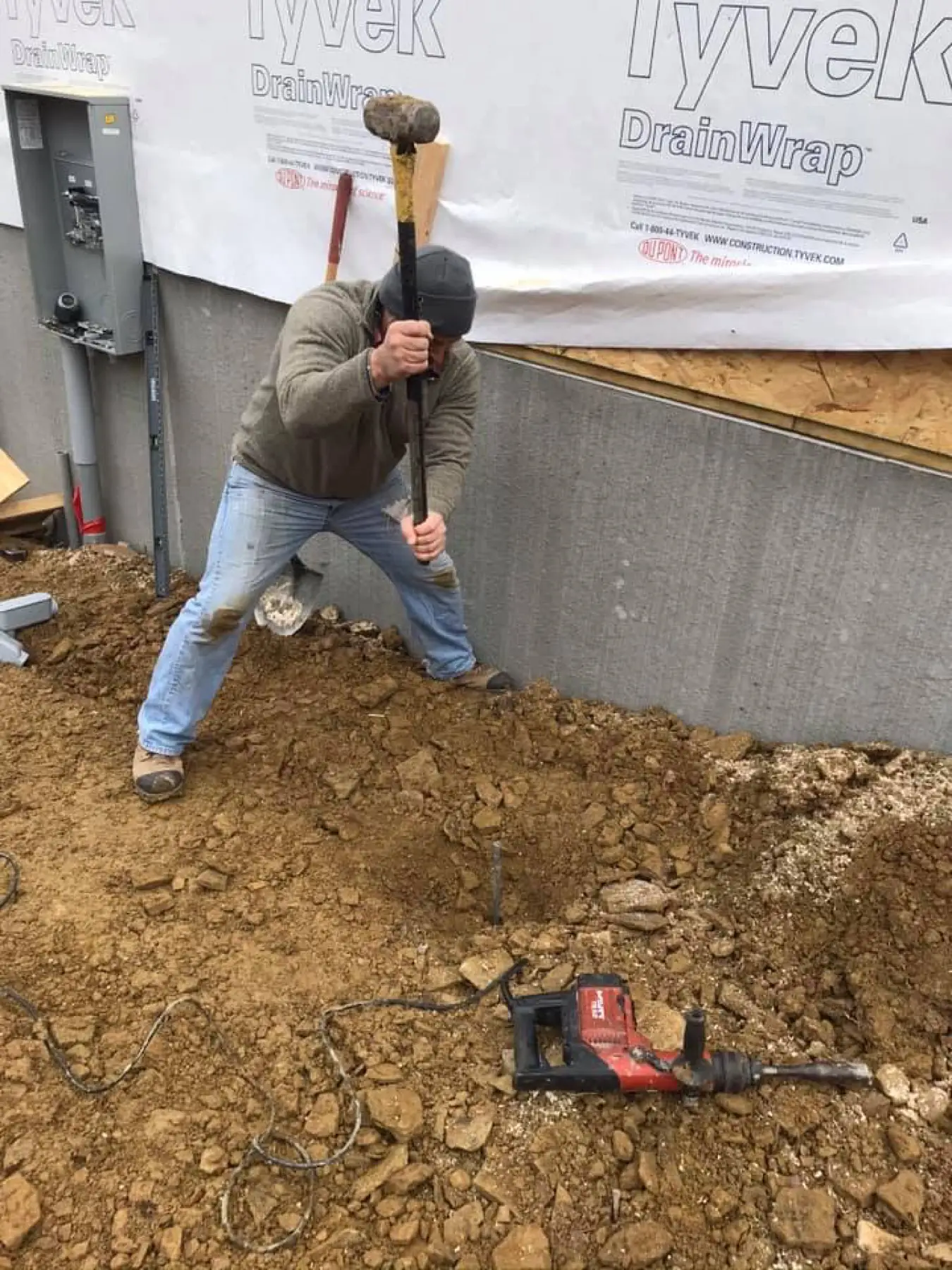 Worker digging a trench along a foundation for underground conduit.