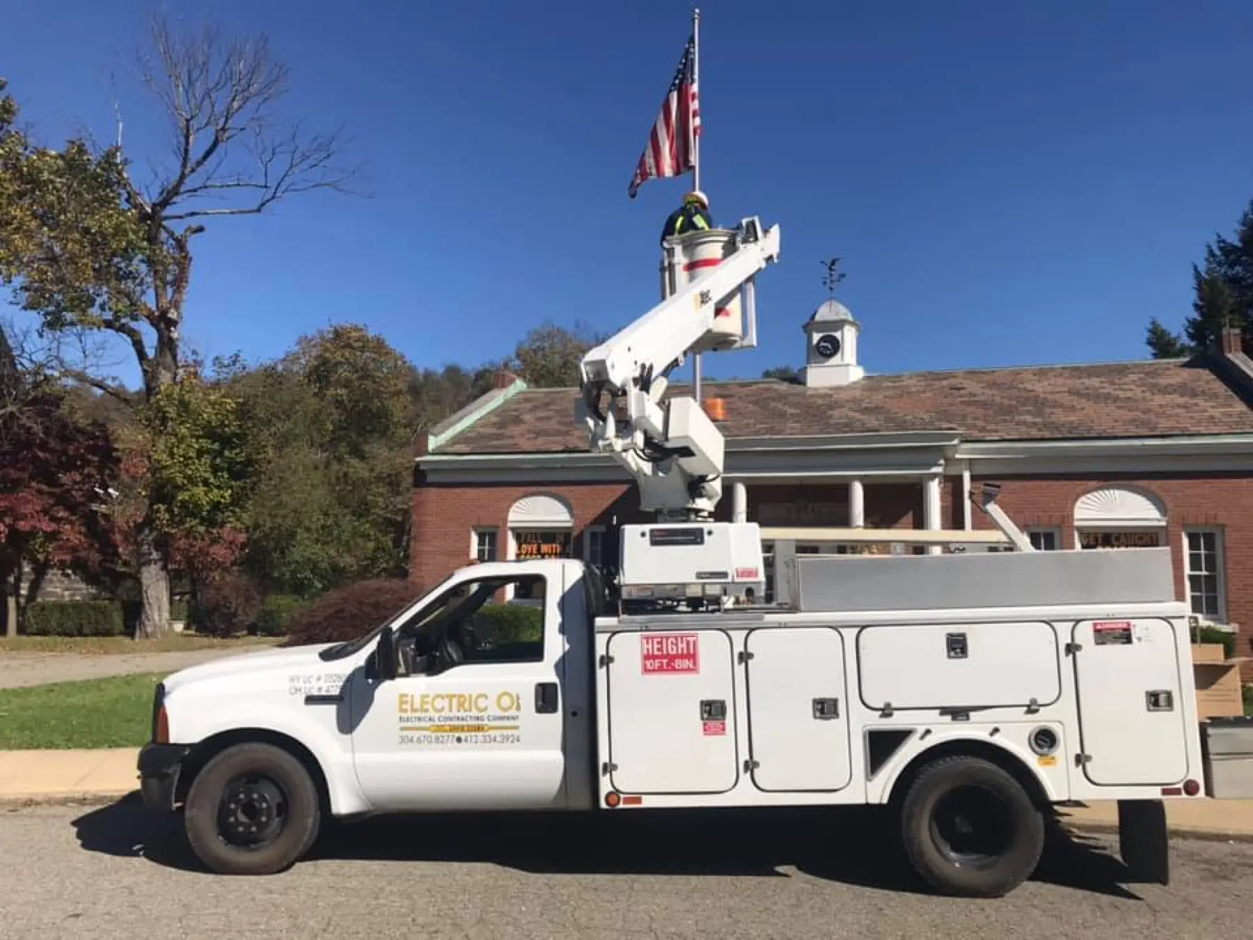 Electric O's bucket truck parked in front of a brick building flying the American flag.