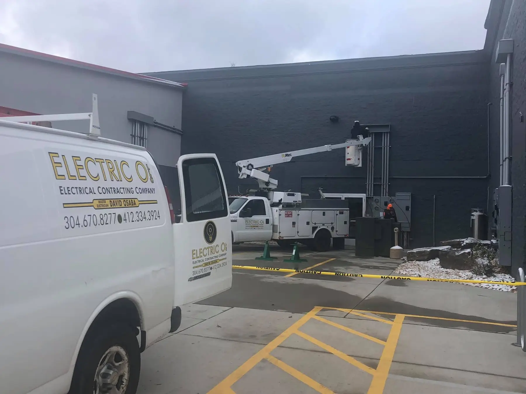Service van and bucket truck working on the exterior of a dark commercial building.